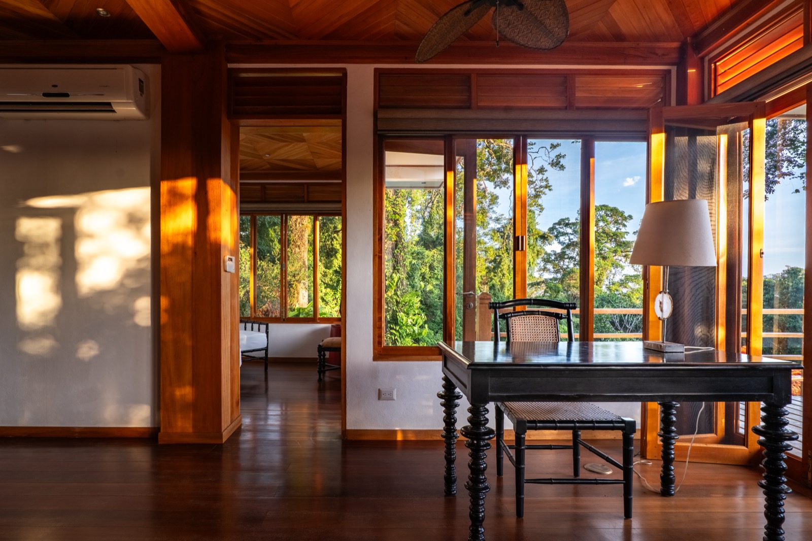 Wood-paneled study with desk and jungle view at sunset